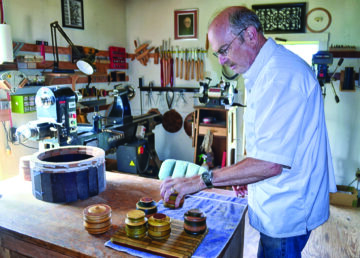 John Young stands at a table on which are placed a collection of round wooden boxes of his making.