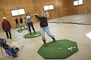 Taylor LaBlanc (foreground) draws back her club at an indoor driving range Friday.  North Country Union High School girls golf Coach Brian Hampton said he has used this space for years to get his practices in during the unpredictable month of April.  From right to left, and in descending order, are: Lindsey Brownfield, Katie Goulet, and Carley Gerioux.  Mr. Hampton is at far left.
