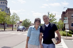 Laura Dolgin, who was recently hired as Newport’s next city manager, poses with her husband, Rick Geisel, on Main Street.  Behind the couple are two buildings that have been, and will be, important in her working life.  At left is the Orleans County Courthouse where she served as county clerk, and on the right is Newport’s Municipal Building, where she will start work on July 20.  Photo by Joseph Gresser