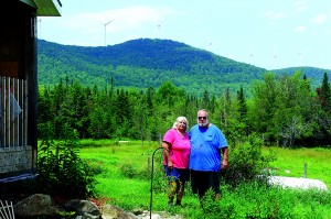 Rita and Paul Martin at their home on the Eden Road in Albany.  The Lowell Mountain turbines dominate the view behind them, though the camera used in this photo was barely able to capture them.  Photo by Chris Braithwaite